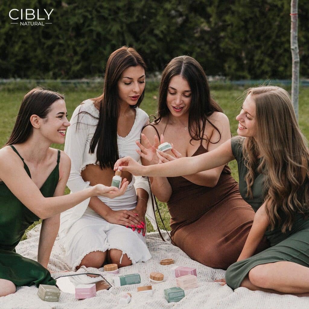 Група жени, седнали на пикник в природата, разглеждат и споделят продукти от органична козметика Cibly.