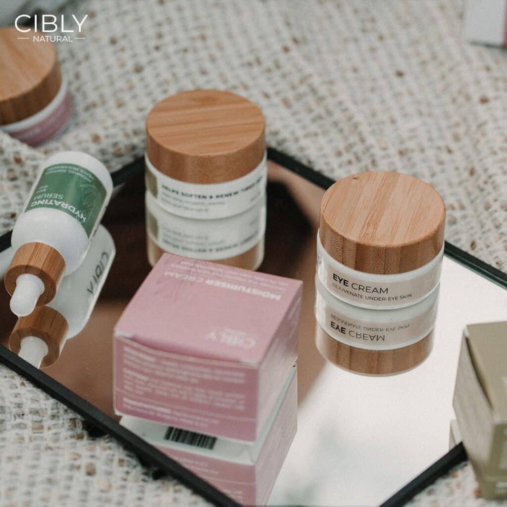 Натурални козметични продукти на Cibly върху огледална повърхност, включващи кремове и серуми в елегантни опаковки с дървени капачки.