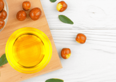 Златисто масло от жожоба в стъклено шише на фона на зелени листа жожоба